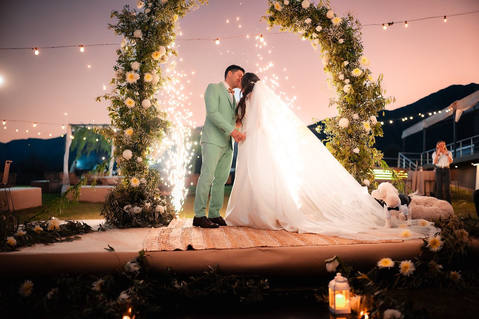 Beso de los novios bajo el arco de flores con bengalas